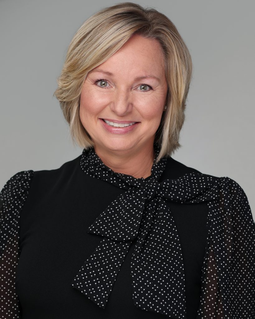 Headshot of Kelly Dawsey wearing a black blouse against a gray background.