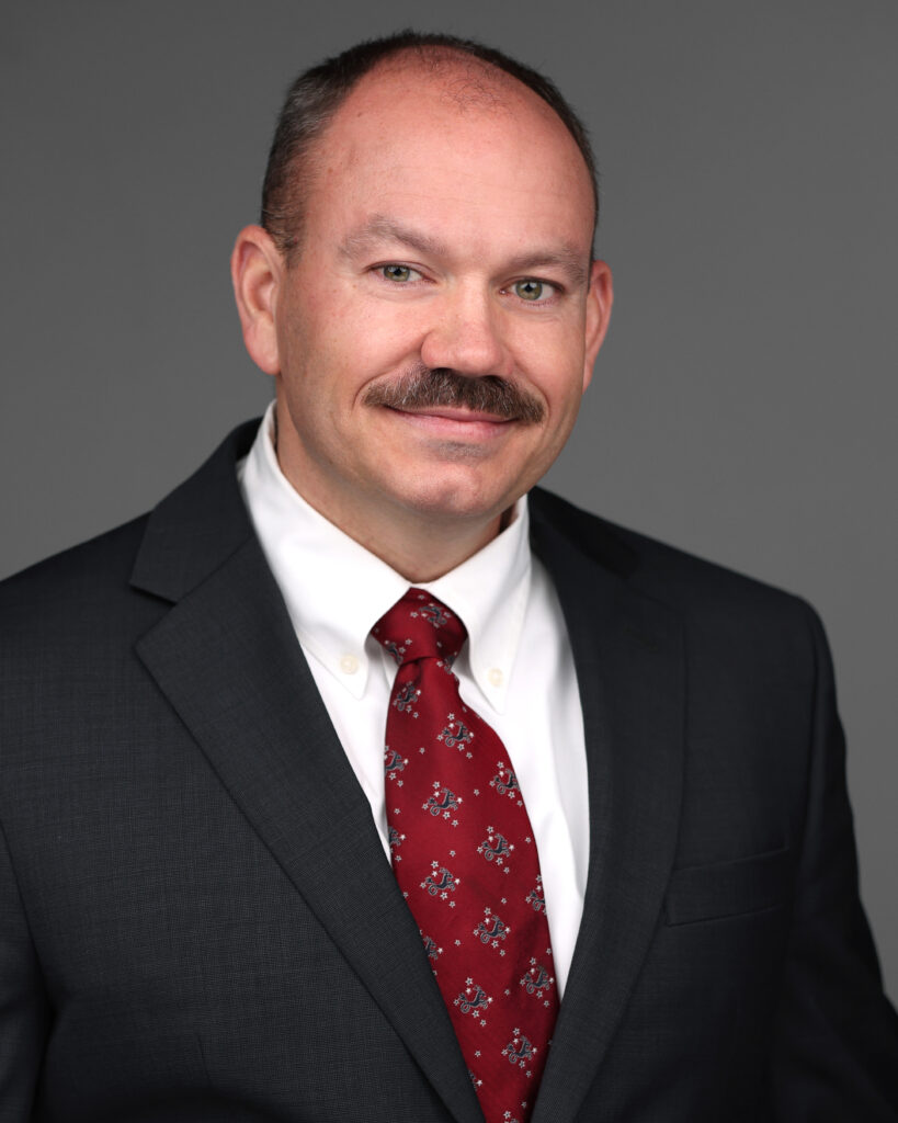 Headshot of Jack Salvato wearing a dark suit, white shirt, and patterned red tie.