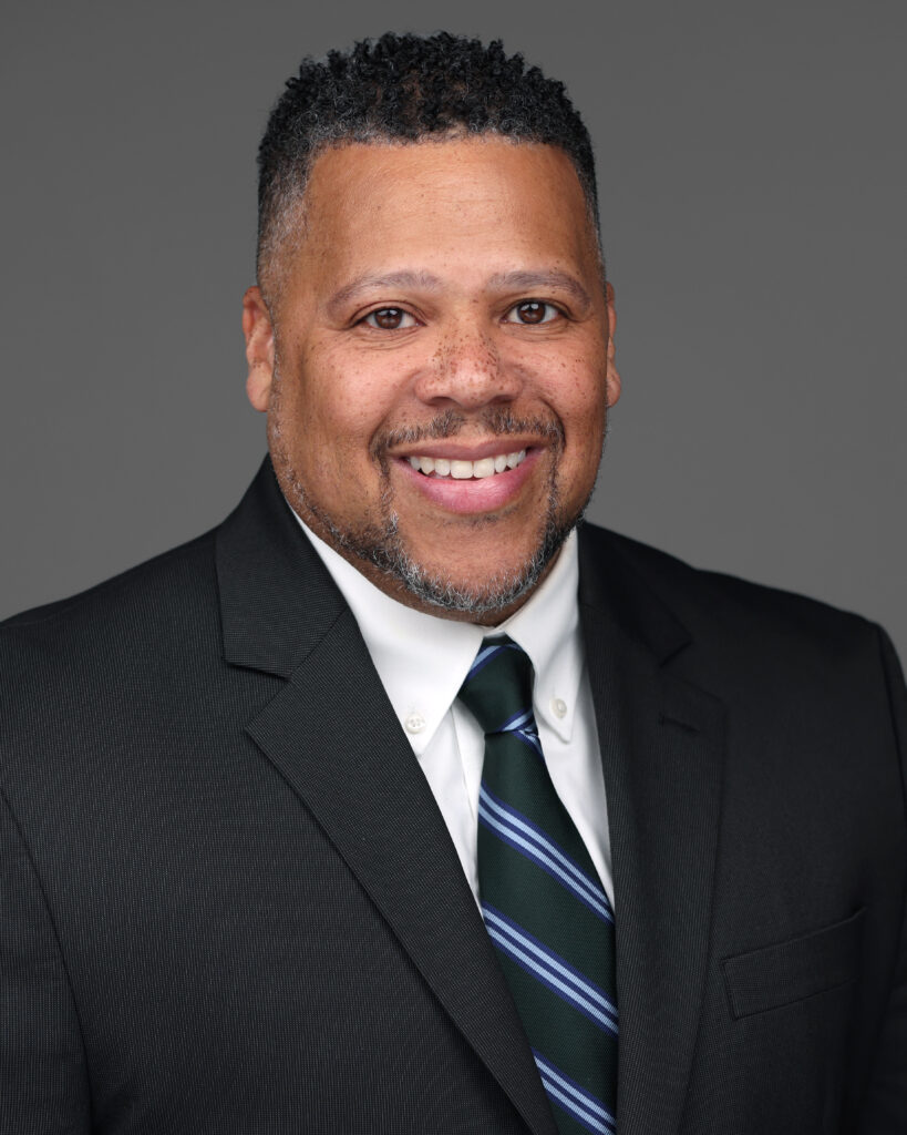 Headshot of CCO Devin Judd wearing a dark suit, white shirt, and striped, blue tie.
