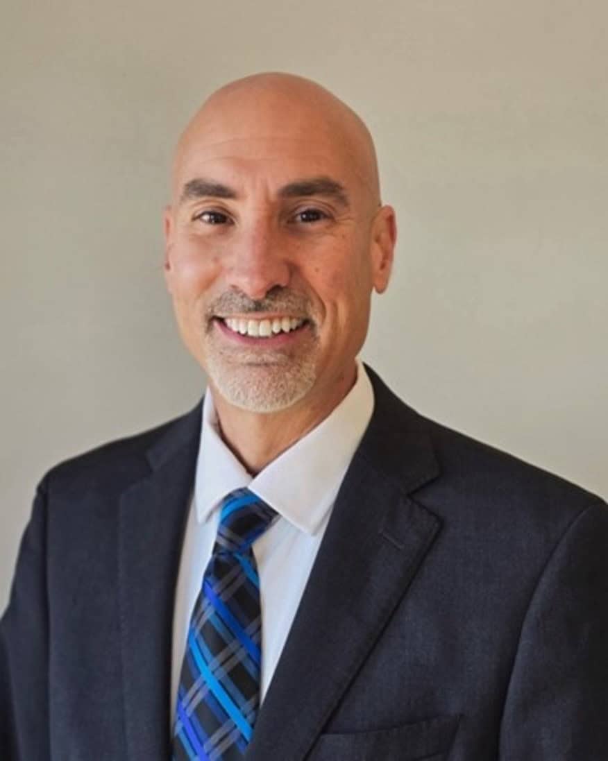 Professional headshot of GSP Chief of Police William Petty smiling at the camera, wearing a dark suit jacket, white dress shirt, and blue patterned tie against a light neutral background.