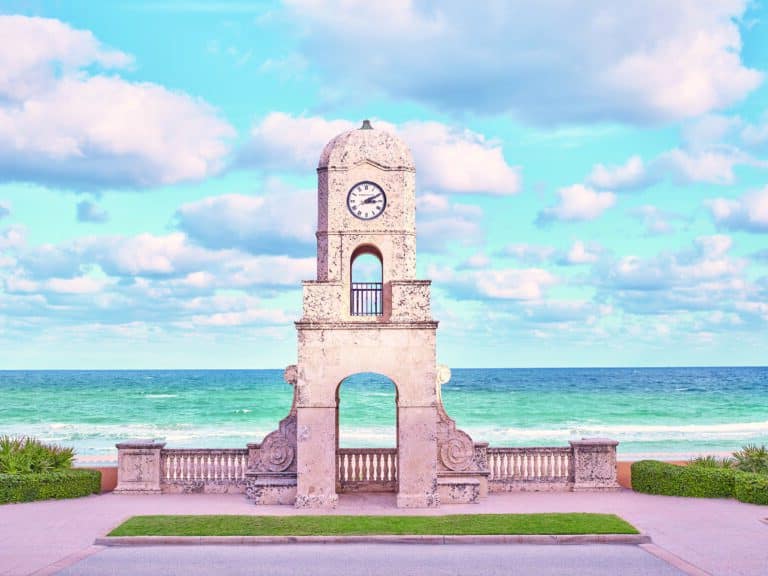 Palm Beach Clock Tower overlooking the Atlantic Ocean, framed by a bright blue sky with scattered clouds.